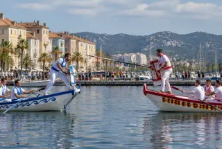 Deux jouteurs provençaux s’affrontent sur des barques dans un port de la rade de Toulon, sous le regard du public.